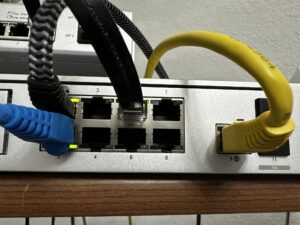 416040575_7823246964358201_2931089499329777331_n - A DataRoad - A DataRoad Network switch with blue and yellow Ethernet cables plugged into ports, showing port numbers and cables in use.