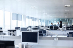hot-desk - A DataRoad - A DataRoad Open-plan office with rows of desks and computer monitors; a small group of three coworkers chatting at the far end.